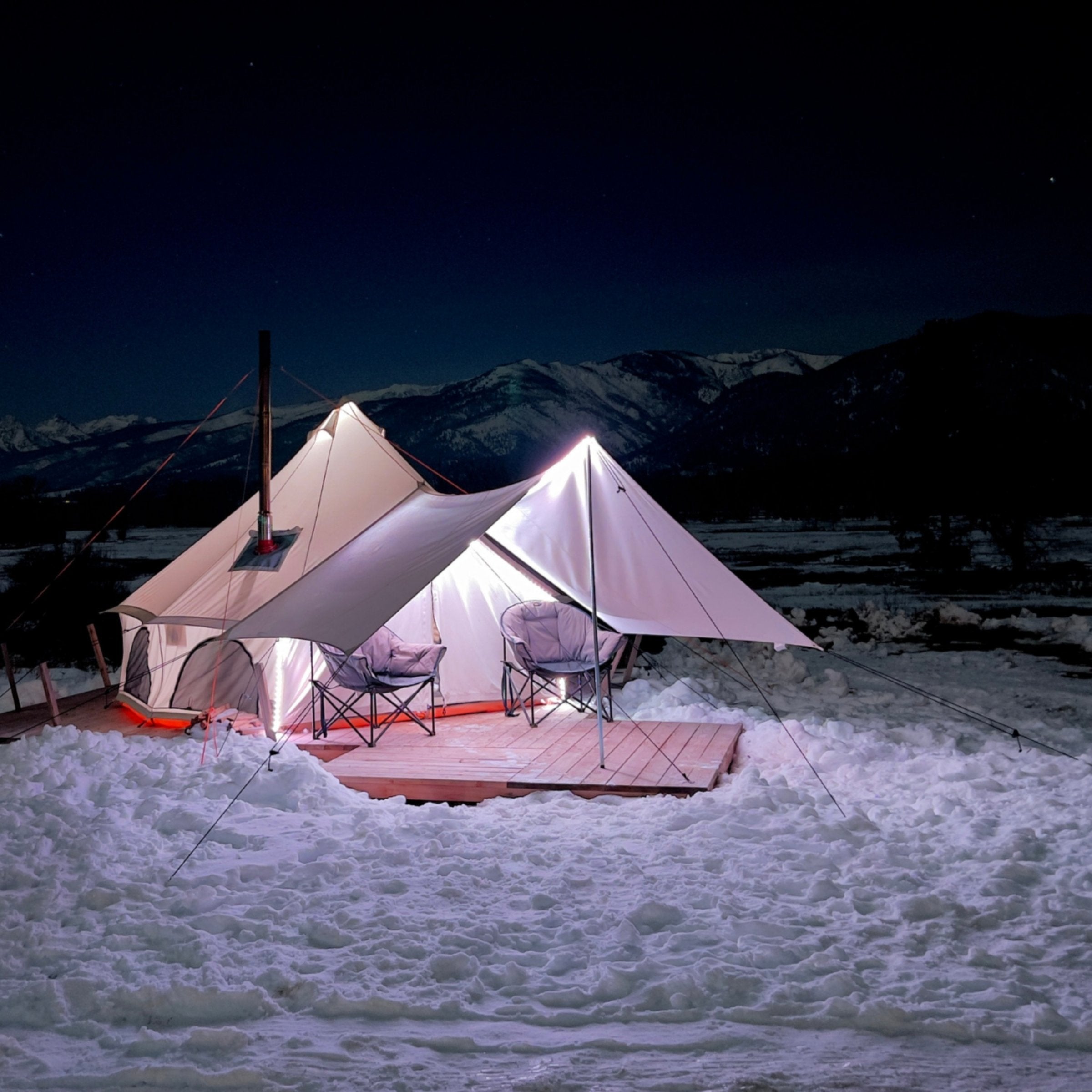 Avalon bell tent set outdoors in a lot of winter snow with camping stove chimney coming out through the tent stove jack
