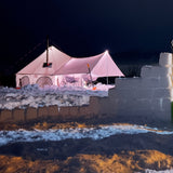 avalon bell tent in a snowy area with lights on and a chimney in the stove jack and ice bricks in front