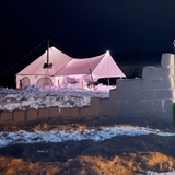 avalon bell tent in an snowy area with lights on and a chimney in the stove jack and ice bricks in front