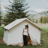 alpha wall tent placed outdoors with a girl standing at its door smiling