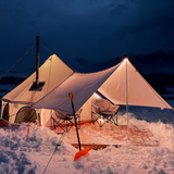 avalon bell tent set up in the snow with lights glowing inside and a stove chimney coming out of the stove jack