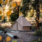 beige 10' Regatta Bell Tent is setup and placed in a forest setting with a tree and greenery