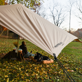 A man is resting under the sunshade tarp with his dog enjoying the weather.
